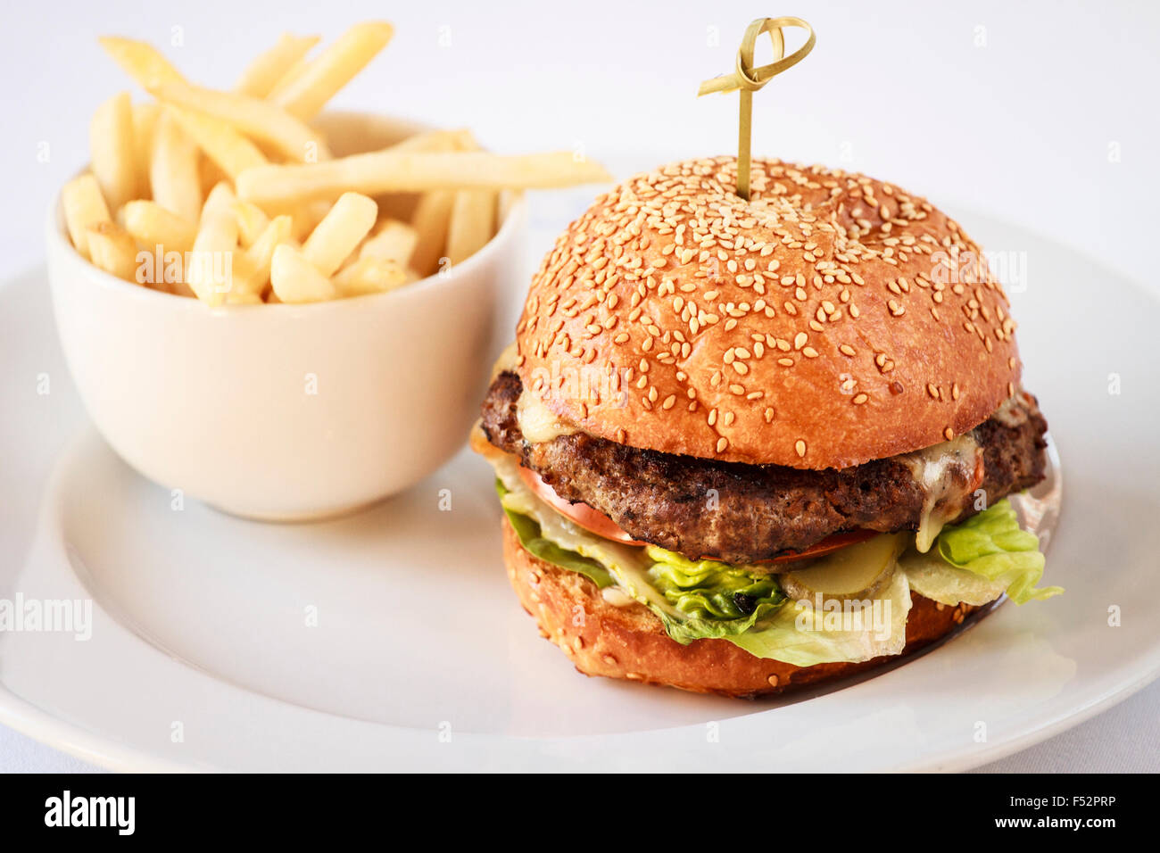 Beef-Burger in einem Sesam Brötchen mit einer Portion Pommes Frites auf einem weißen Teller Stockfoto