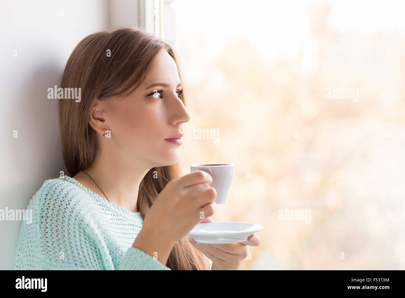 Junge Frau Kaffeetrinken in der Nähe des Fensters an sonnigen Tag. Ziemlich  Erwachsene denken Mädchen hält Tasse Espresso und Durchsicht w  Stockfotografie - Alamy