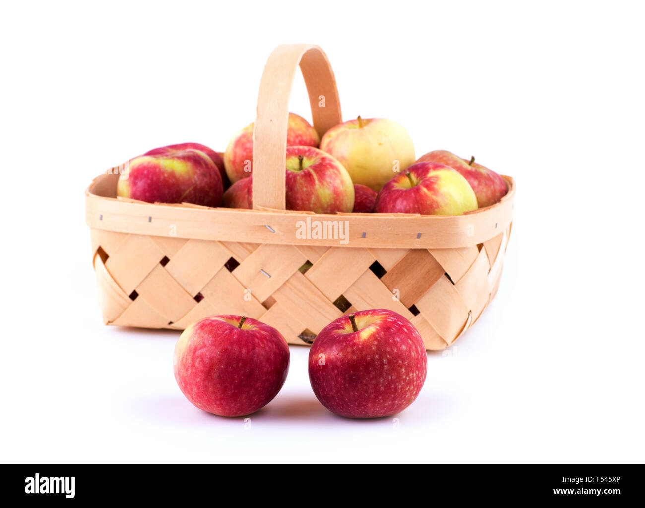Zwei Äpfel vor einem hölzernen Korb voller mehr Äpfel auf weiß Stockfoto