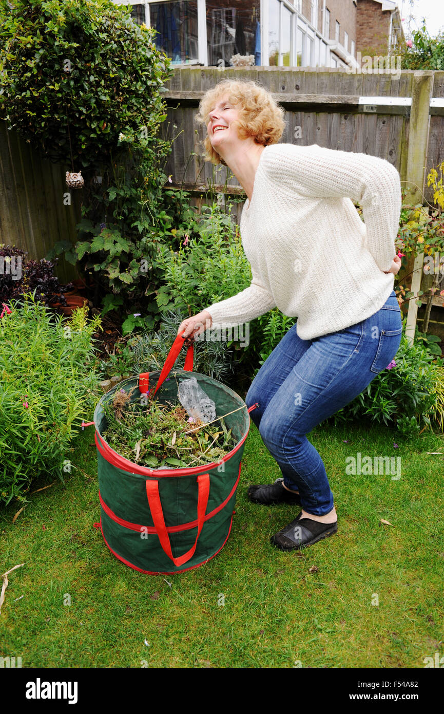Reife Frau im Garten schwere Hebesack von Gartenabfällen Schmerzen bei einer schlechten Rückenschmerzen Stockfoto