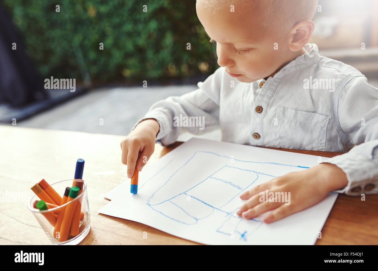 Kleiner Junge unterhalten sich auf einen heißen Sommer Tag stehend an einem Tisch auf einer Terrasse im freien Zeichnung mit farbigen Buntstiften auf Blatt Stockfoto