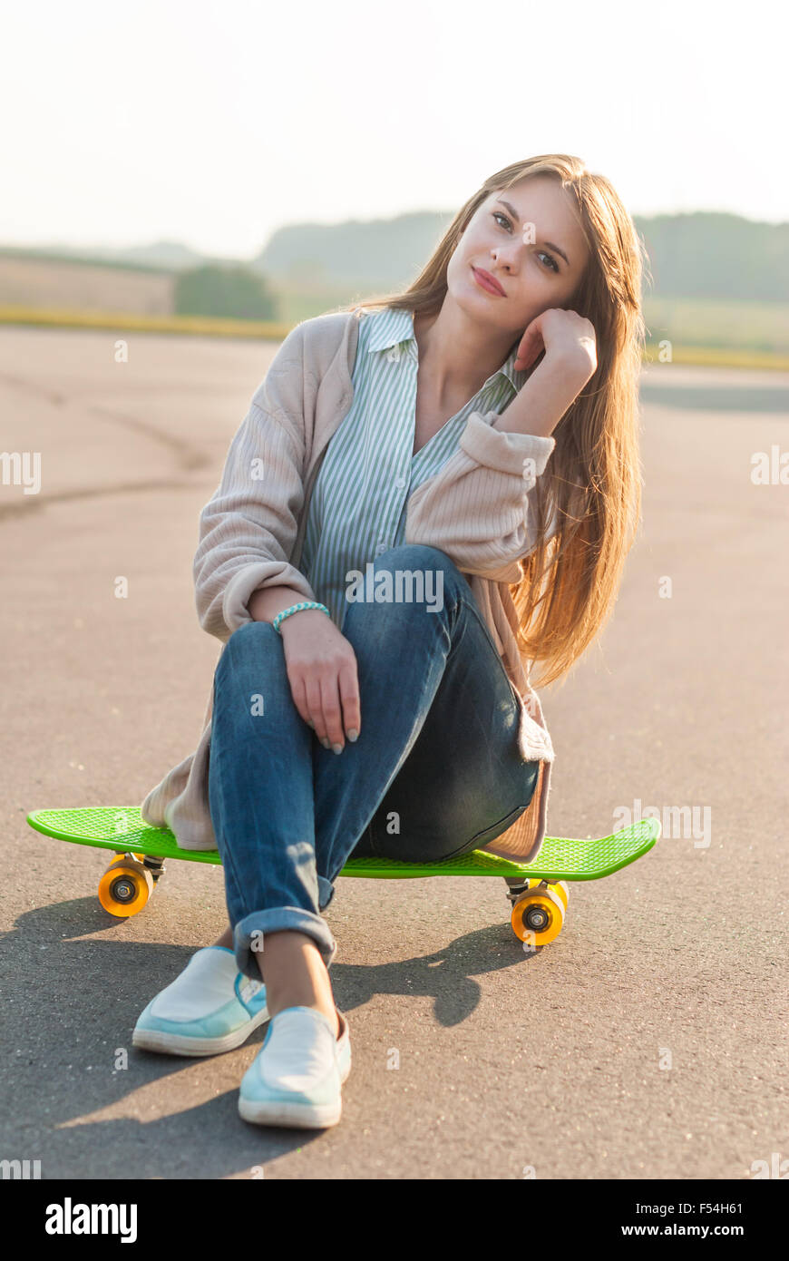 Junges Mädchen sitzt auf einem Skateboard auf der Straße. Stockfoto