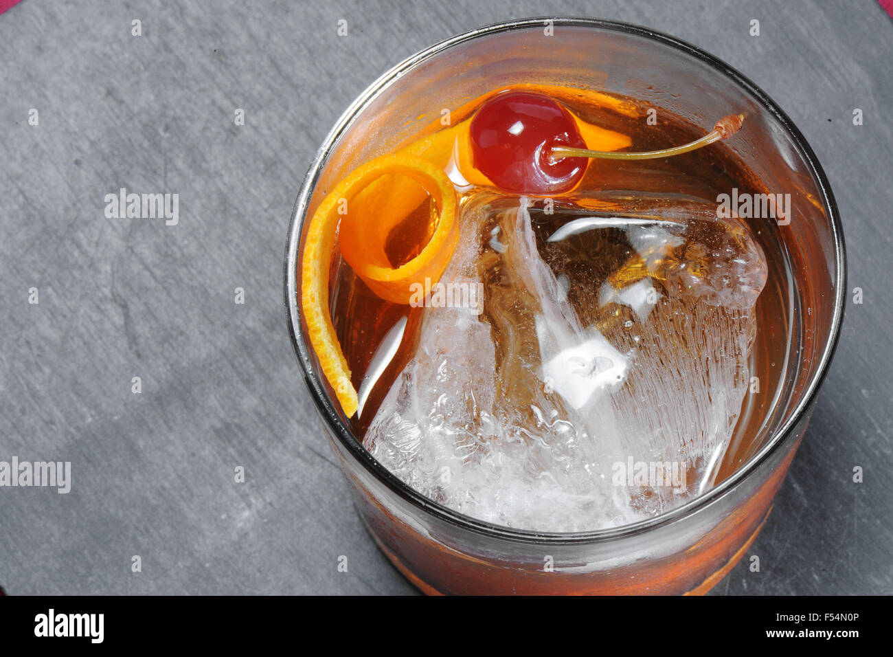Ein Glas Gin mit Eis, Orangenschalen und eine Kirsche. Stockfoto