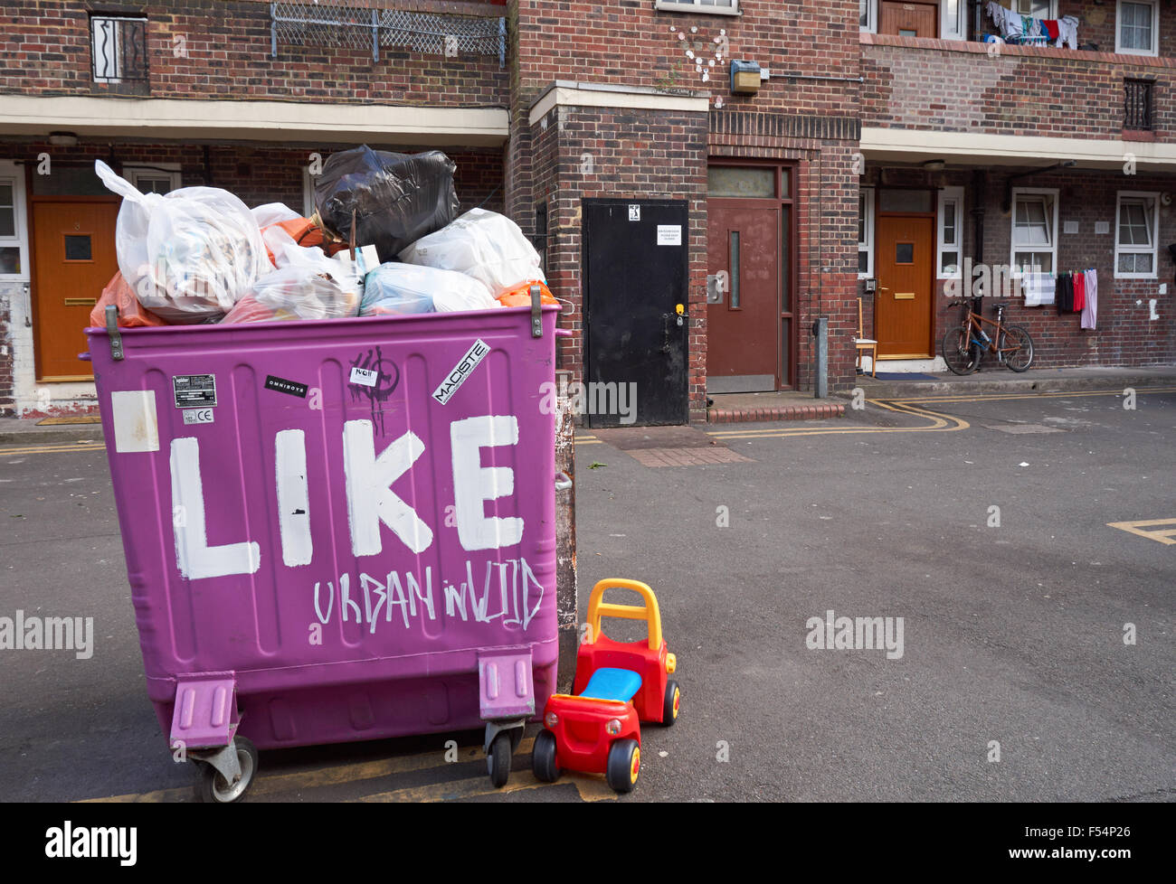 Große lila Wheelie bin mit Sozialwohnungen im Hintergrund in London England Vereinigtes Königreich UK Stockfoto