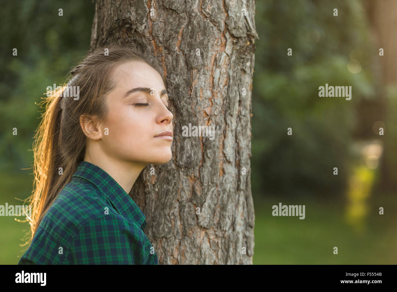 Schöne Frau mit Augen geschlossen stützte sich auf Baumstamm im park Stockfoto