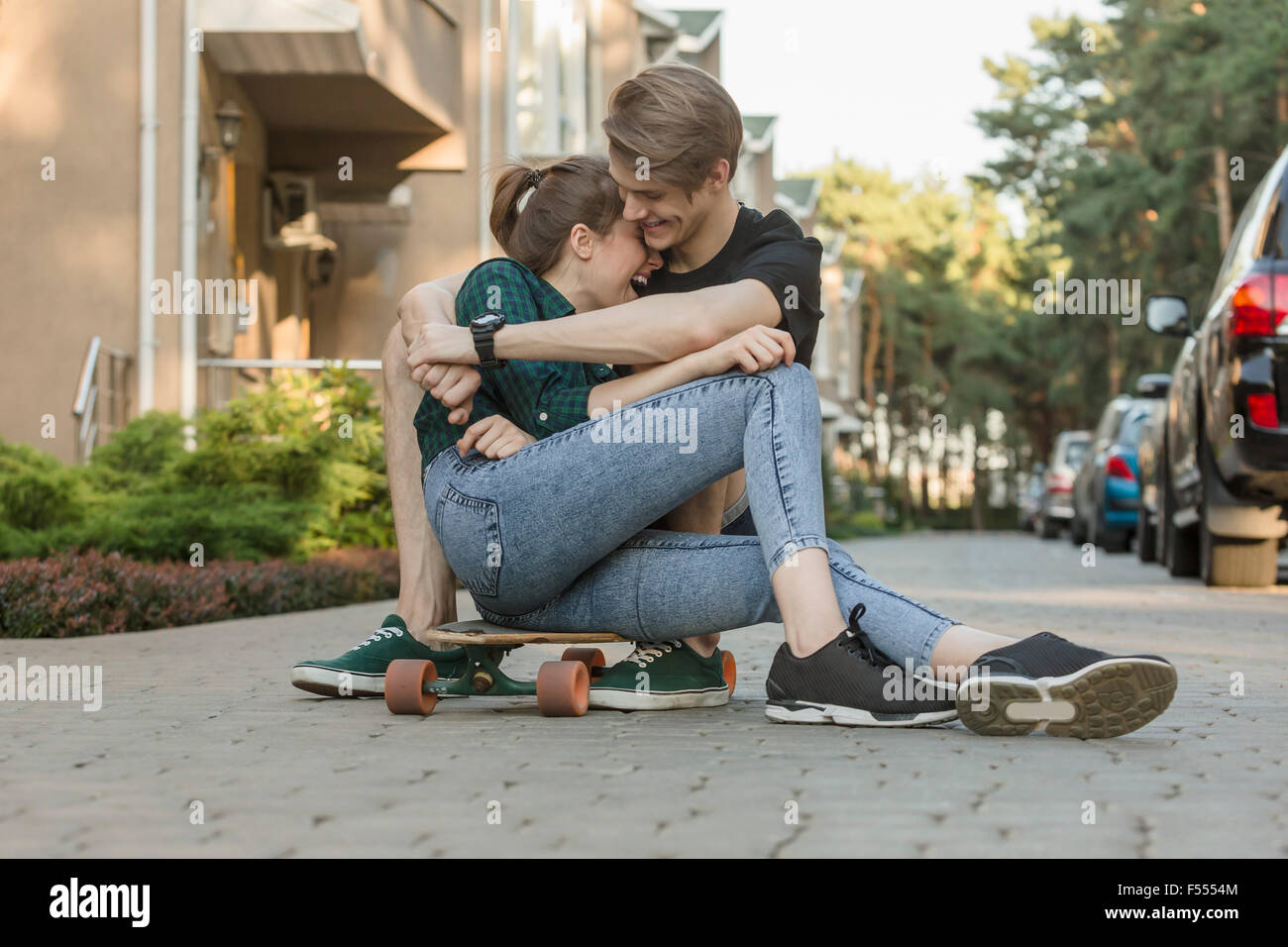 Glückliches junges Paar auf Skateboard im freien sitzend umarmen Stockfoto