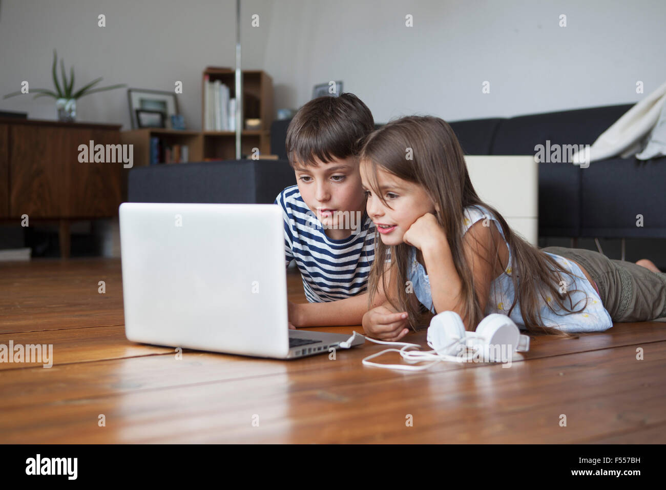 Geschwister mit Laptop auf dem Parkett zu Hause Stockfoto