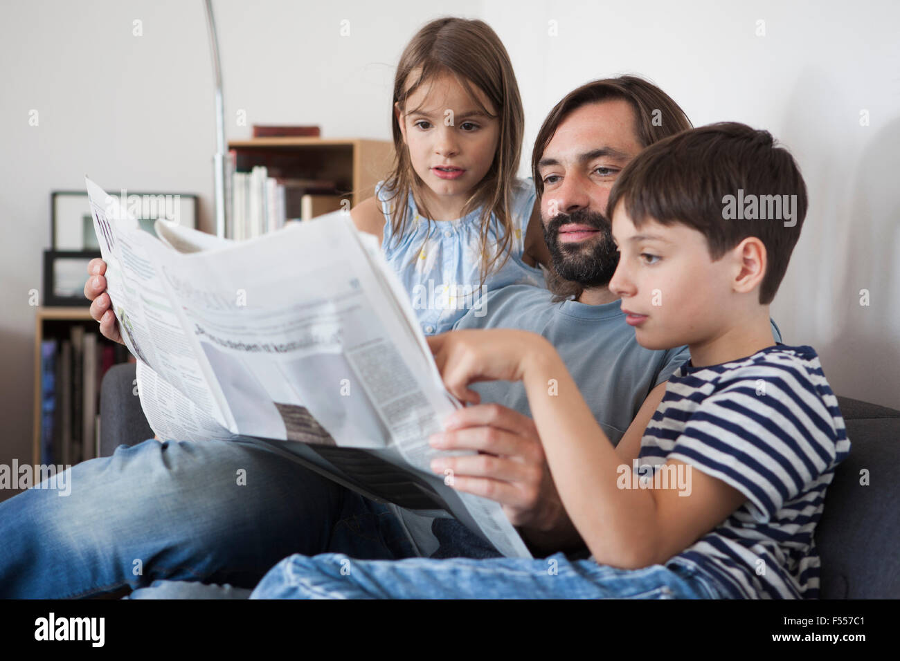 Vater und Kinder lesen Zeitung zu Hause auf sofa Stockfoto