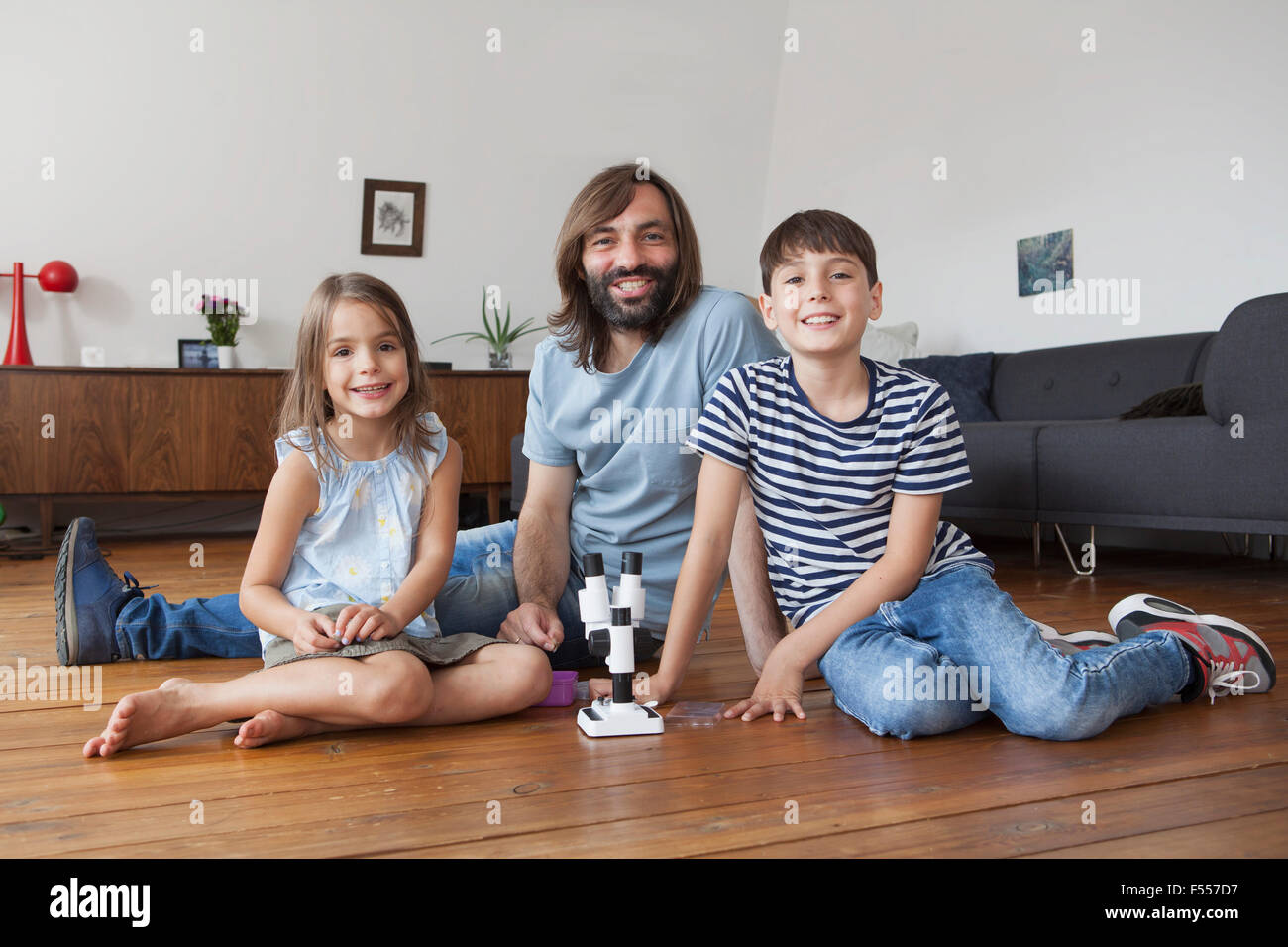 Porträt von Vater und Kindern mit Mikroskop auf Boden zu Hause sitzen Stockfoto
