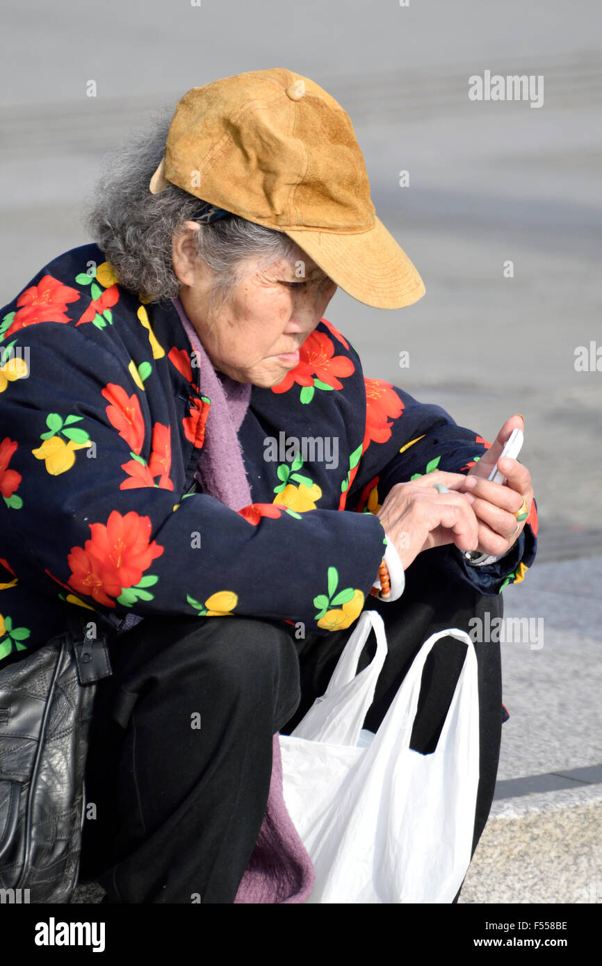 London, England, Vereinigtes Königreich. Alte chinesische Frau, Blick auf ihr Mobiltelefon auf dem Trafalgar Square Stockfoto