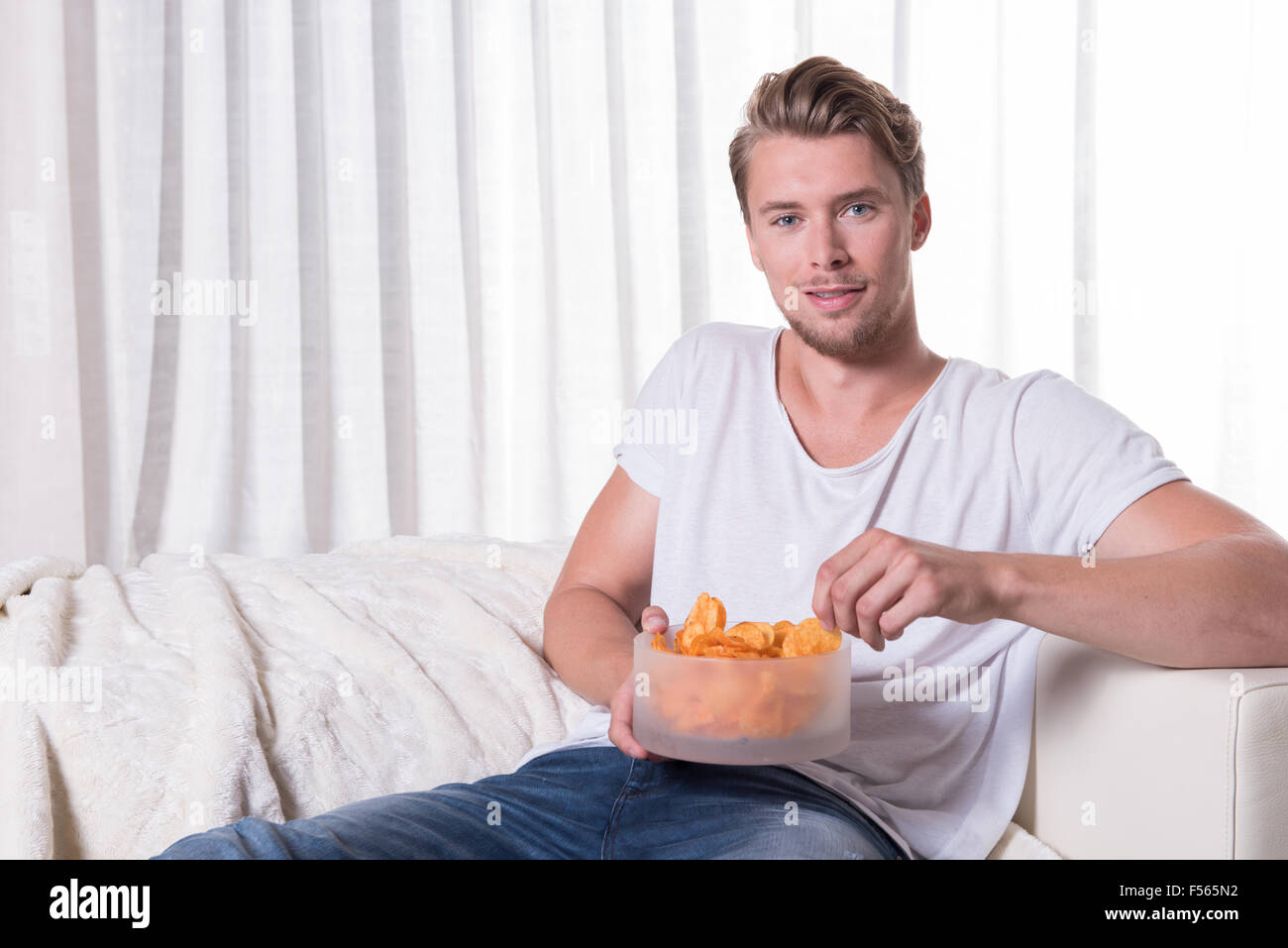 Porträt, junger Mann auf der Couch sitzen und Essen chips Stockfoto