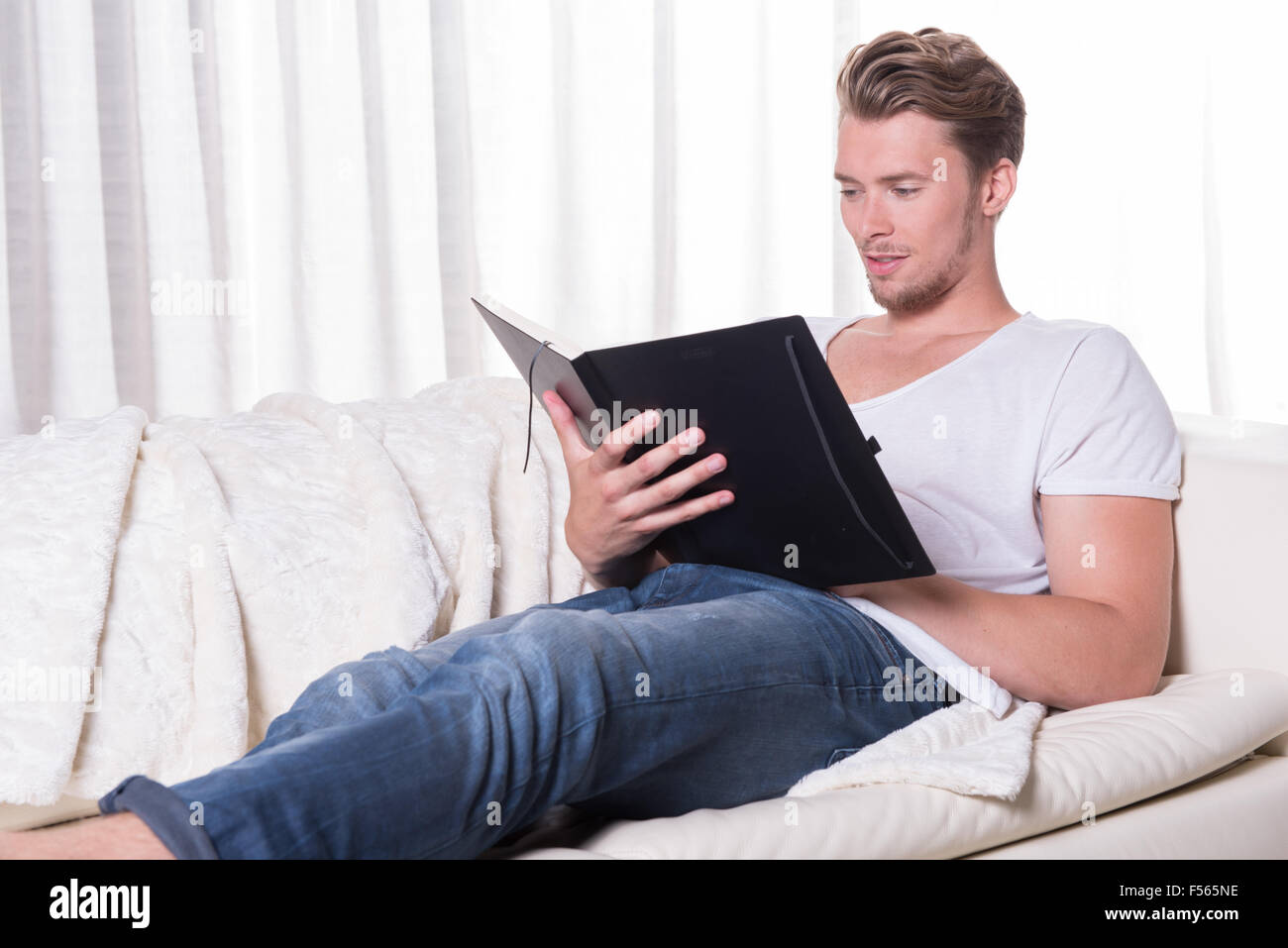 Porträt, junger Mann auf der Couch sitzt und liest in einem Buch Stockfoto