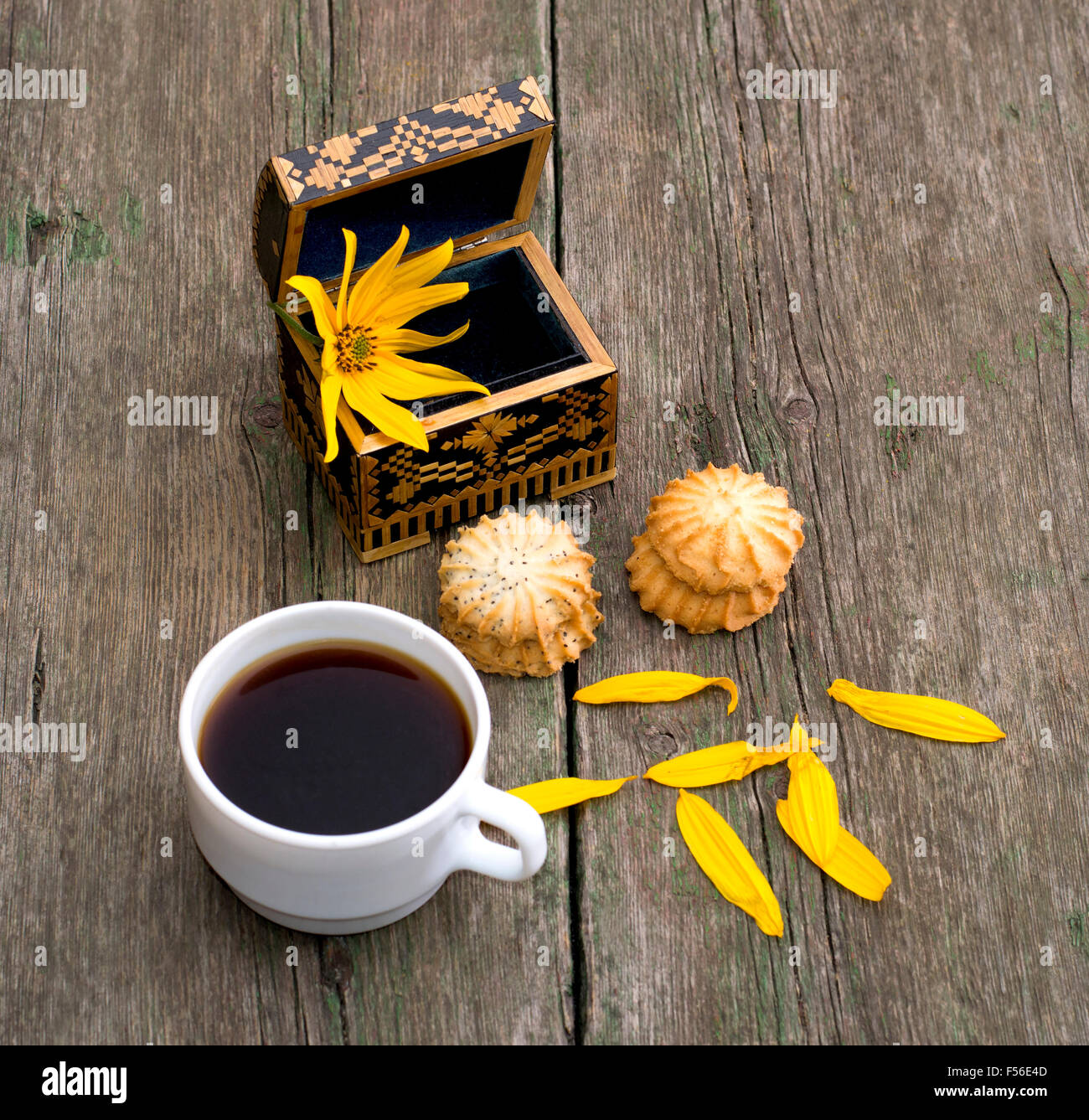 Tasse Kaffee, offenen Sarg mit einer Blume zwei Verknüpfung von Cookies und Blütenblätter, ein Still-Leben auf ein alter Tisch, ein Thema Lebensmittel und dr Stockfoto