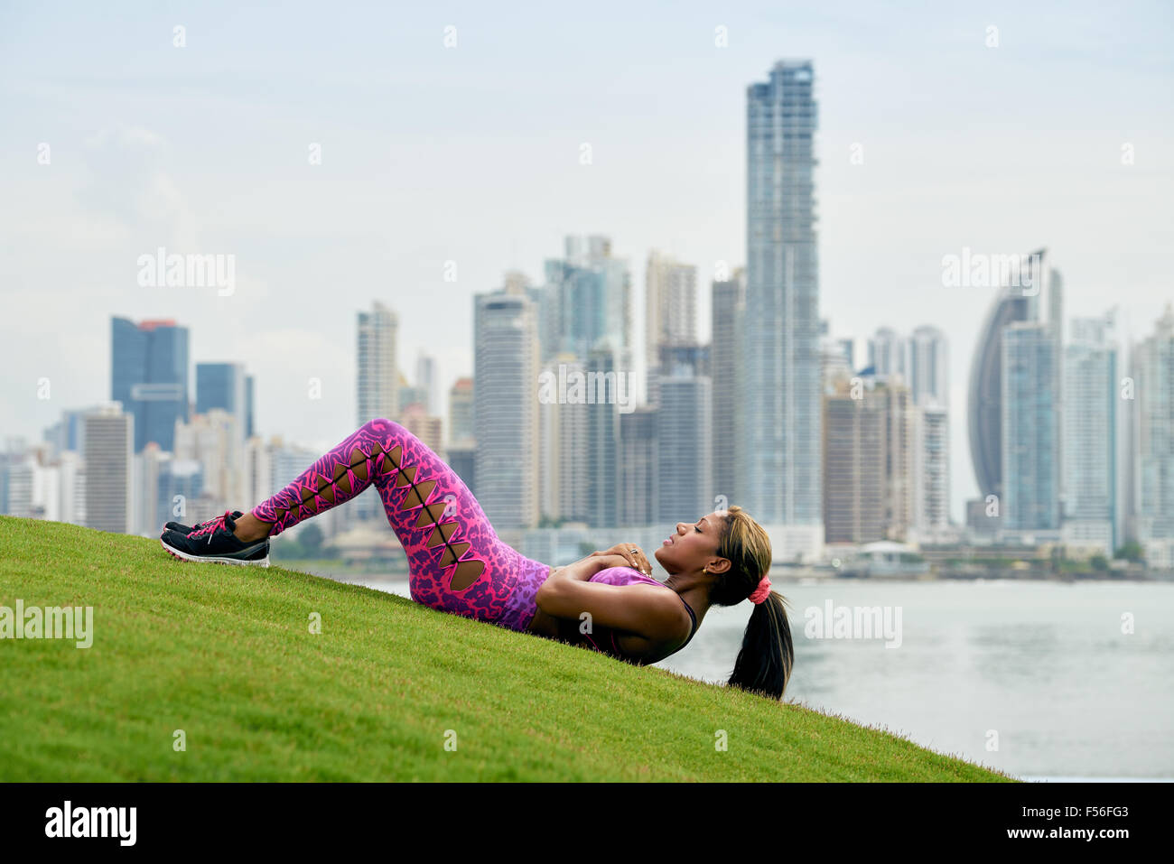 Junge afrikanische Amerikanerin Bauchmuskeln trainieren und trainieren am frühen Morgen in der Stadt. Sie trainiert, auf Rasen entlang der Cinta C Stockfoto