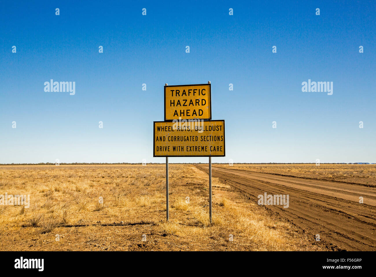 Signieren von australischen outback Road, über baumlose Prärie zum fernen Horizont unter blauem Himmel, Warnung vor Verkehrsrisiko voraus & Straßenzustand Stockfoto
