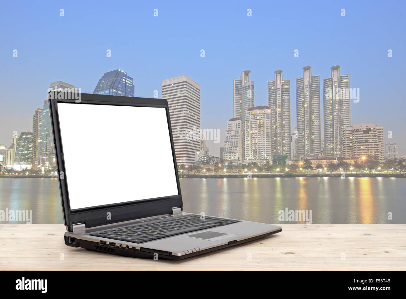Laptop mit leeren Bildschirm auf Holztisch mit hohen Gebäude Hintergrund Stadtbild Konzept Geschäftsidee Stockfoto