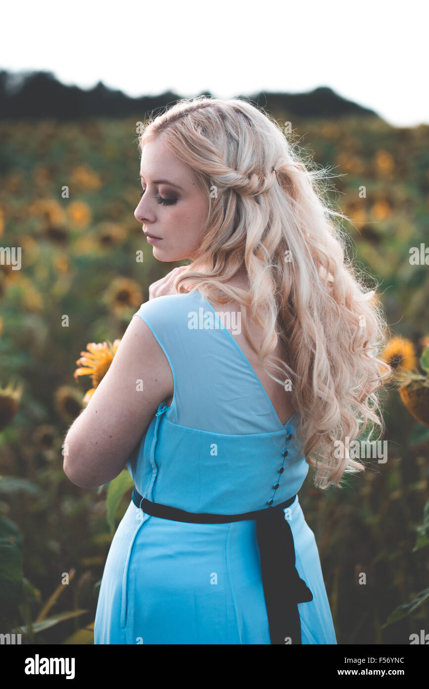 Schöne junge Frau in einem Sonnenblumenfeld an goldene Stunde Stockfoto