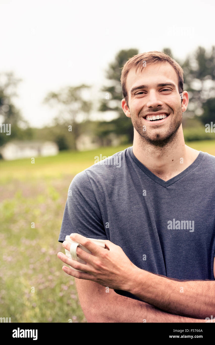 Ein junger Mann hält ein Kaffee Tasse steht in einem Feld am See. Stockfoto