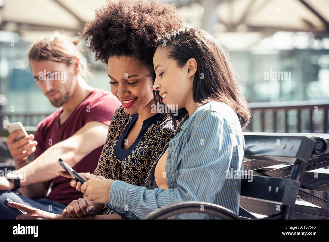 Drei Personen sitzen nebeneinander auf einer Parkbank Überprüfung ihres Smartphones Stockfoto