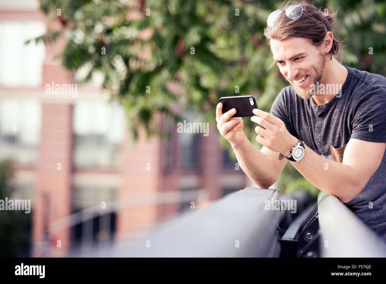 Ein junger Mann stützte sich auf ein Park Geländer prüfen sein Handy Stockfoto