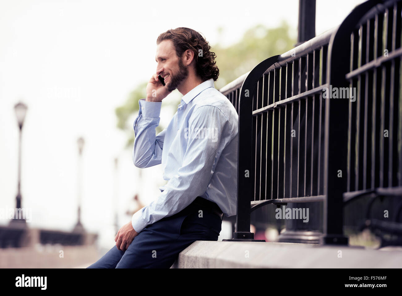 Ein Mann sitzt auf einem Schritt auf der Straße einen Anruf tätigen. Stockfoto