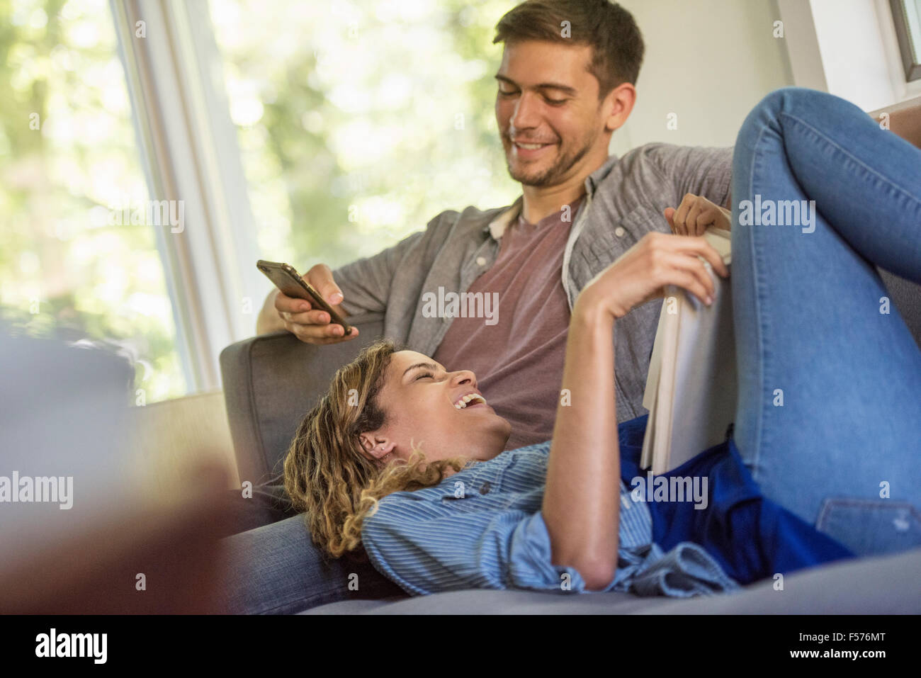 Ein paar, einen Mann Überprüfung sein Telefon und eine Frau liegend ein Buch lesen. Stockfoto