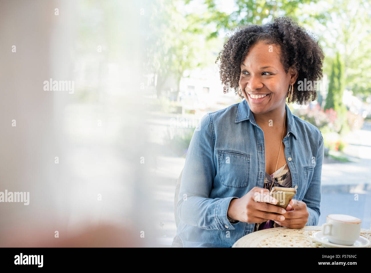 Eine Frau hält ihr Smartphone an einem Café-Tisch. Stockfoto