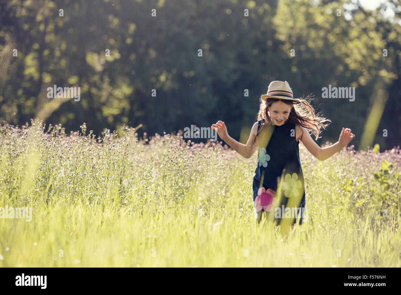 Ein Kind, ein junges Mädchen im Strohhut auf einer Wiese von wilden Blumen im Sommer. Stockfoto