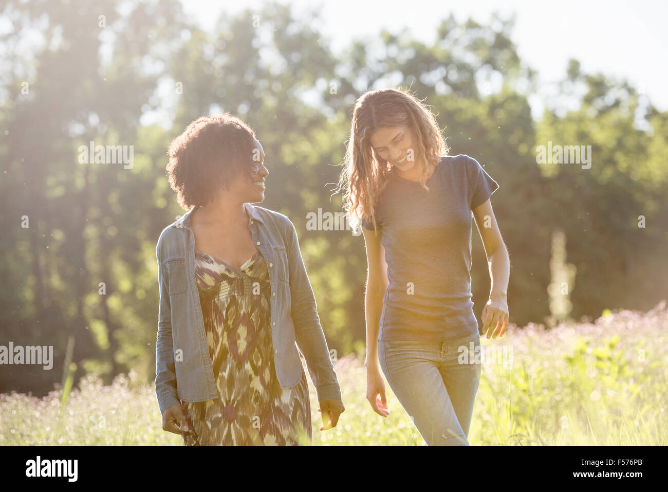 Zwei Frauen zu Fuß durch ein Feld reden und lachen. Stockfoto