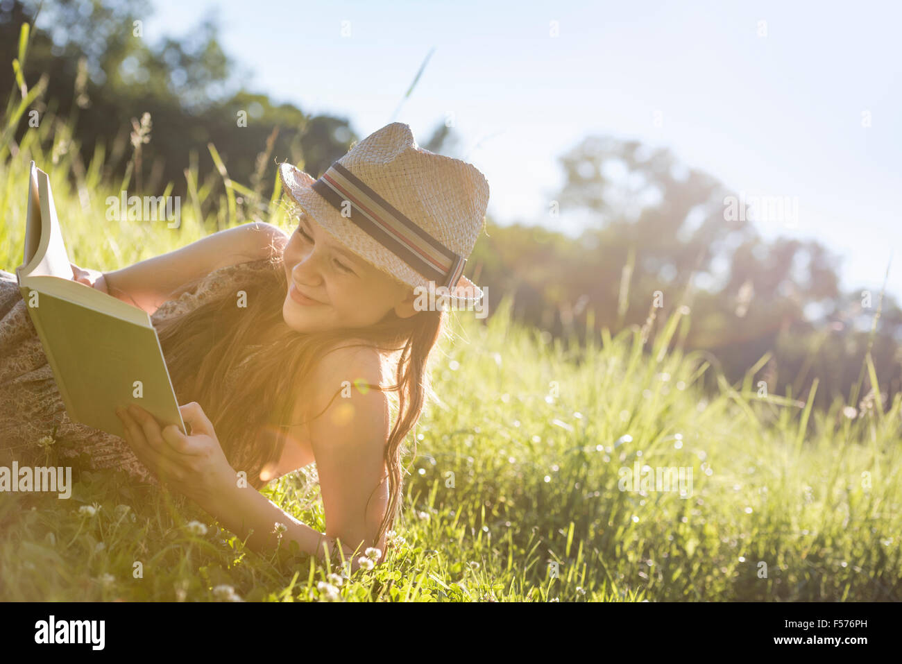 Ein junges Mädchen in einem Strohhut liegen auf dem Rasen, ein Buch zu lesen. Stockfoto