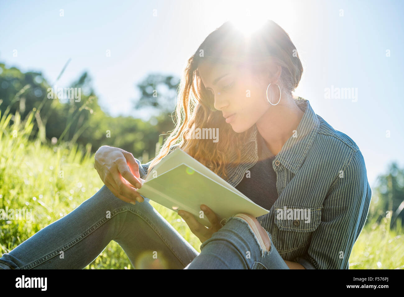 Eine junge Frau sitzt in der Sonne, ein Buch zu lesen Stockfoto