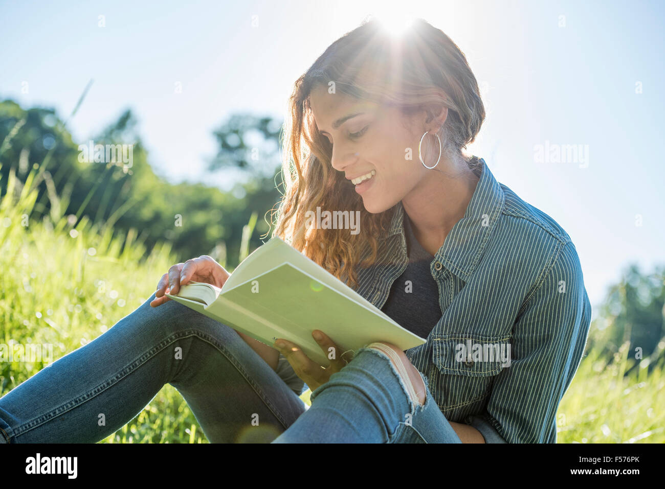 Eine junge Frau sitzt in der Sonne, ein Buch zu lesen Stockfoto
