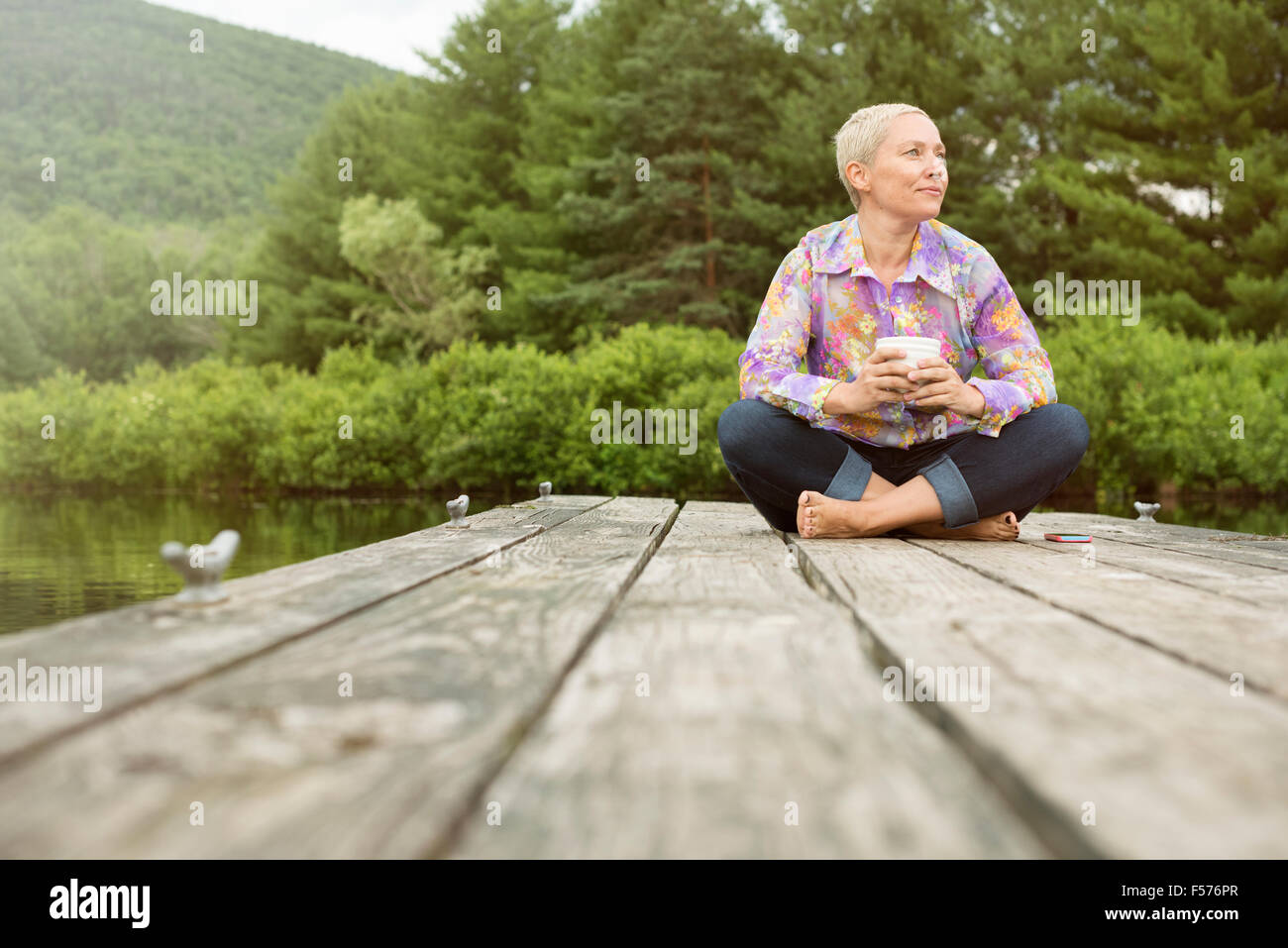 Eine Frau sitzt im Freien auf einem Dock mit einer Tasse Kaffee Stockfoto