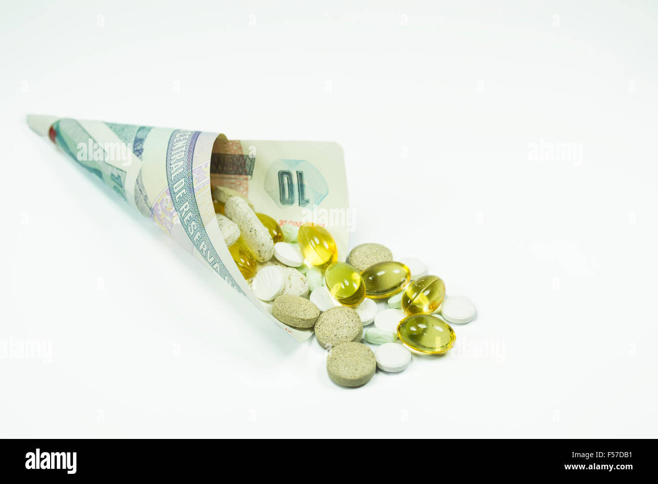 Verschiedene Pillen innerhalb einer Banknote, eingehüllt in eine Kegelform, Konzeptbild über die Kosten des Gesundheitswesens, isoliert auf weiss Stockfoto
