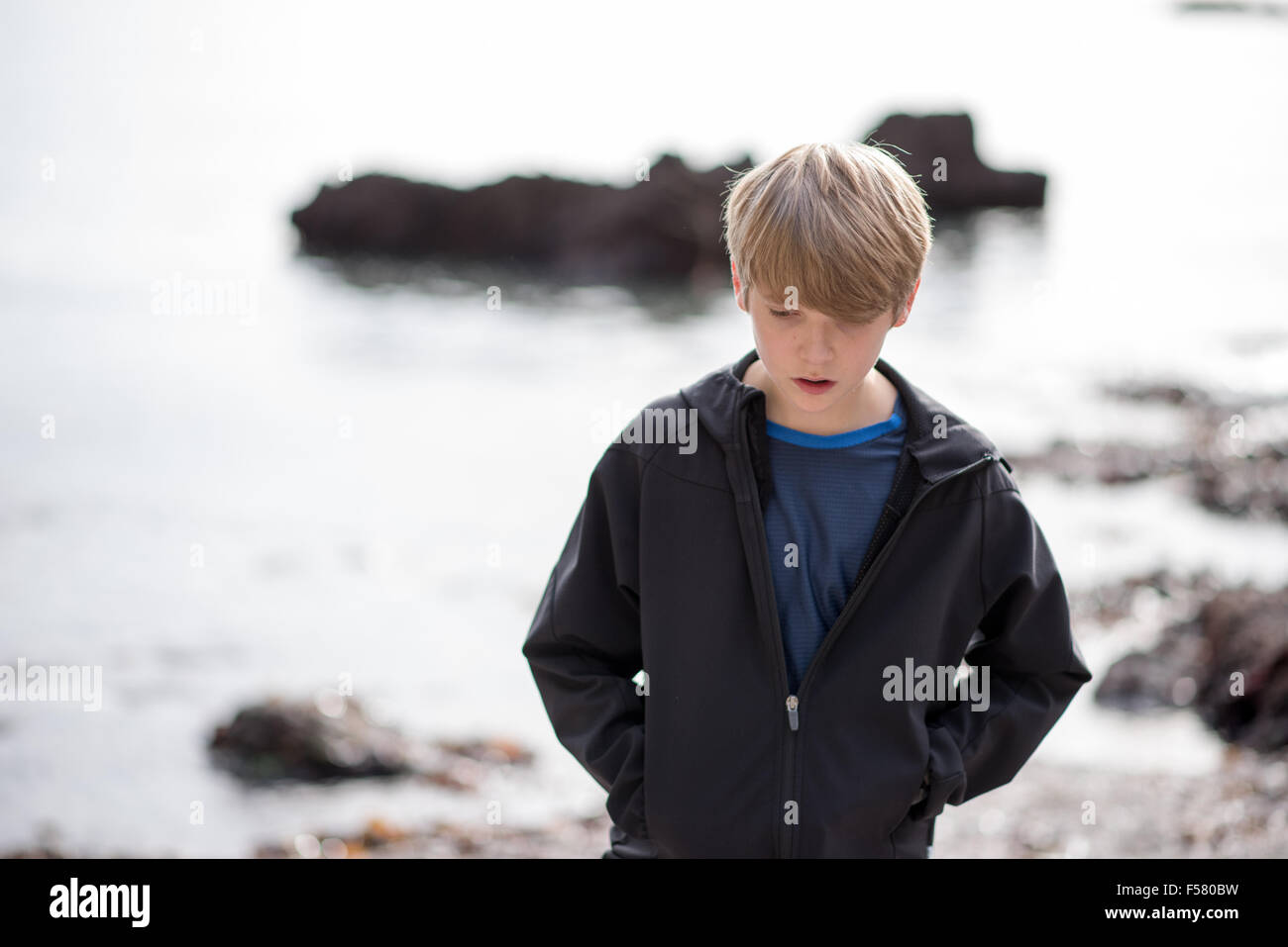 Blonder weiße Teenager in einer schwarzen Jacke geht allein auf einen Strand suchen, traurig und unglücklich in der Herbstsonne Stockfoto