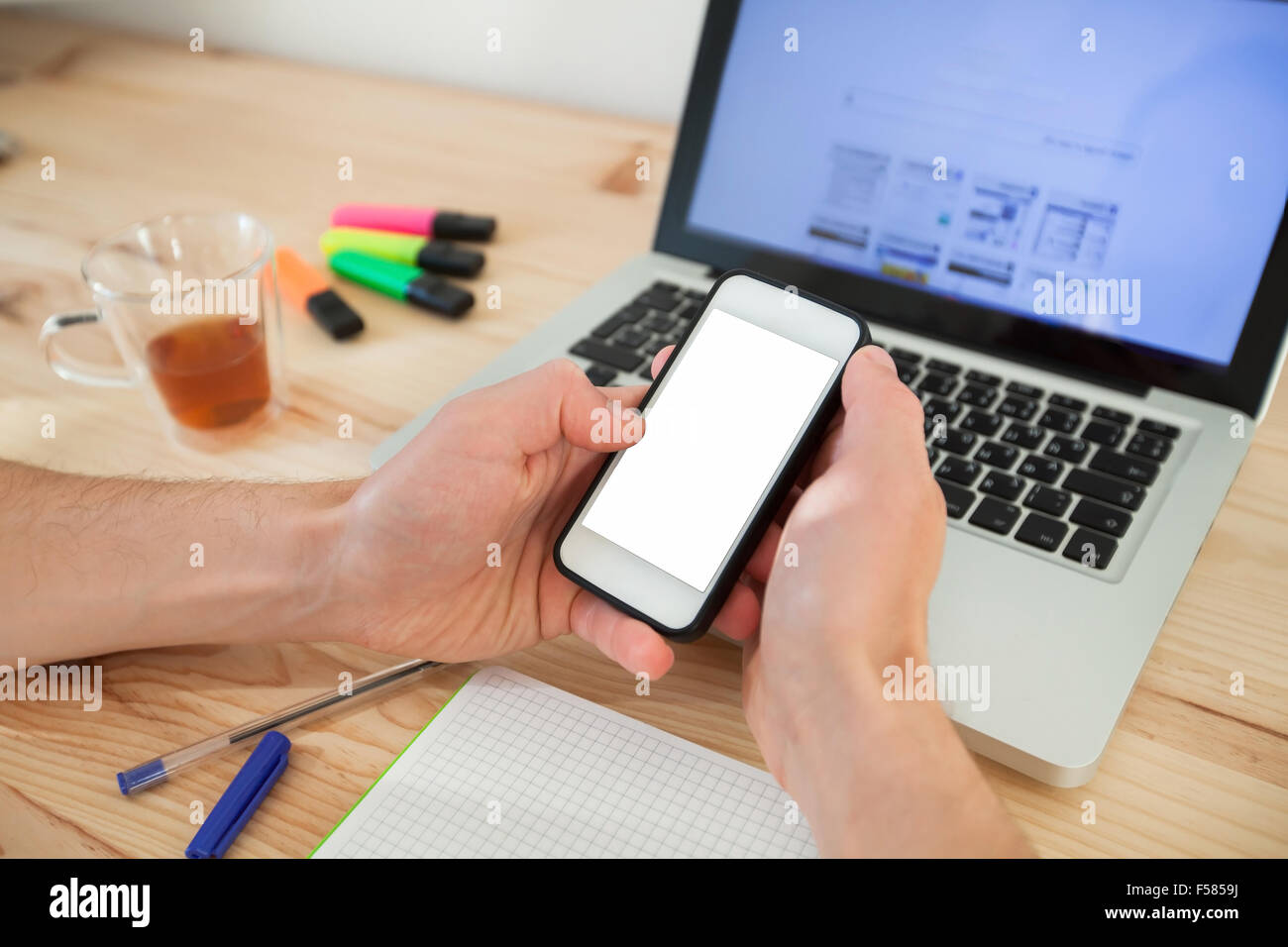 Mann mit Smartphone mit weißen Bildschirm in der Nähe von Laptop im Wohngebäude Stockfoto