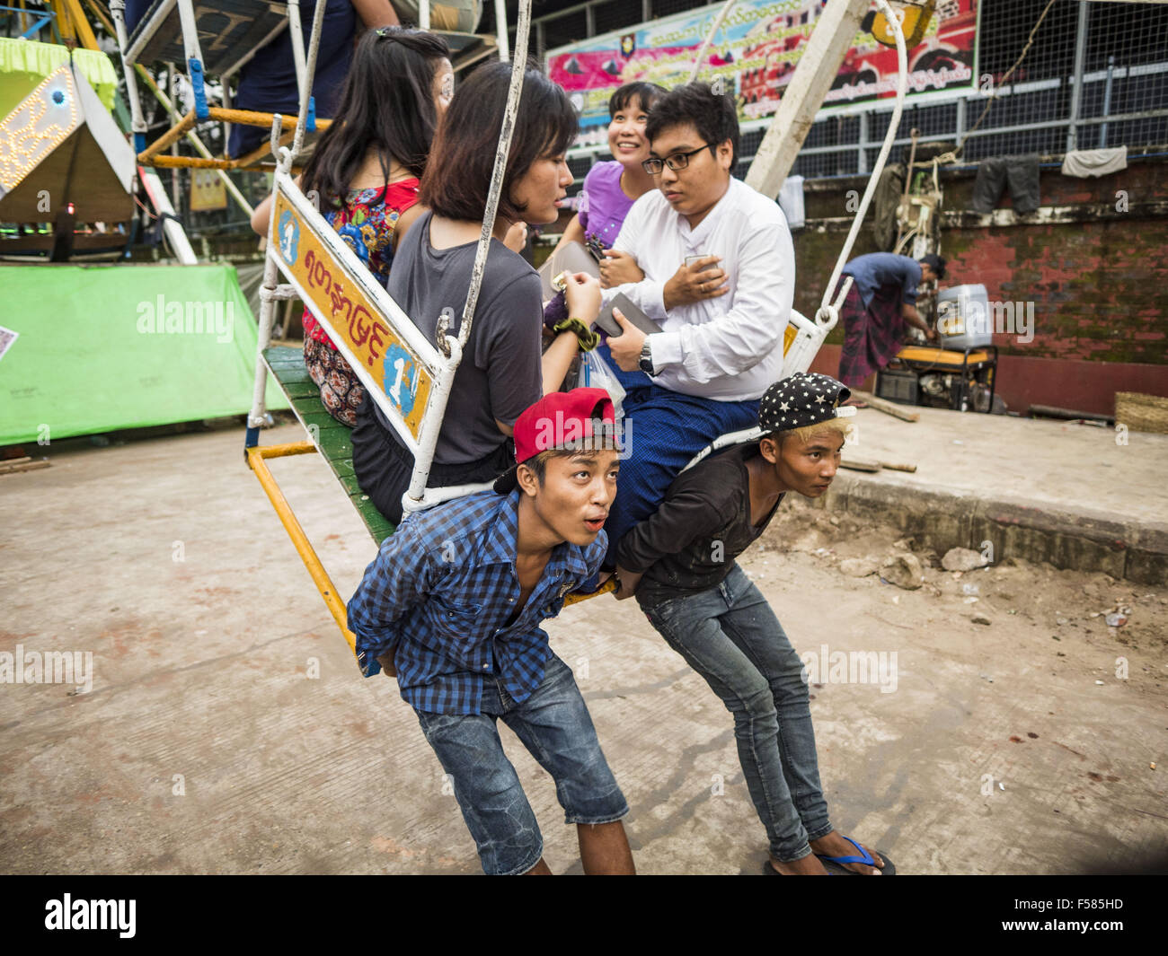 Yangon, Yangon Division, Myanmar. 29. Oktober 2015. Fahren Sie Begleiter auf ein Riesenrad Auto halten beim Straßenkarneval in zentralen Yangon. Strom ist knapp in Myanmar, insbesondere in ländlichen Gebieten, und die meisten Reisen Karneval verwenden menschliche angetriebene Fahrten. Arbeiter Aufstieg an die Spitze des Riesenrads und ziehen ihn dann um daran drehen. Der Karneval fiel zusammen mit dem Thadingyut-Festival, die Beleuchtung Festival von Myanmar, der auf dem gregorianischen Kalender am Vollmondtag des birmanischen lunaren Monats Thadingyut, Oktober oder November begangen wird. Der Karneval vorgestellten Essen, Fahrten und Spiele. Stockfoto