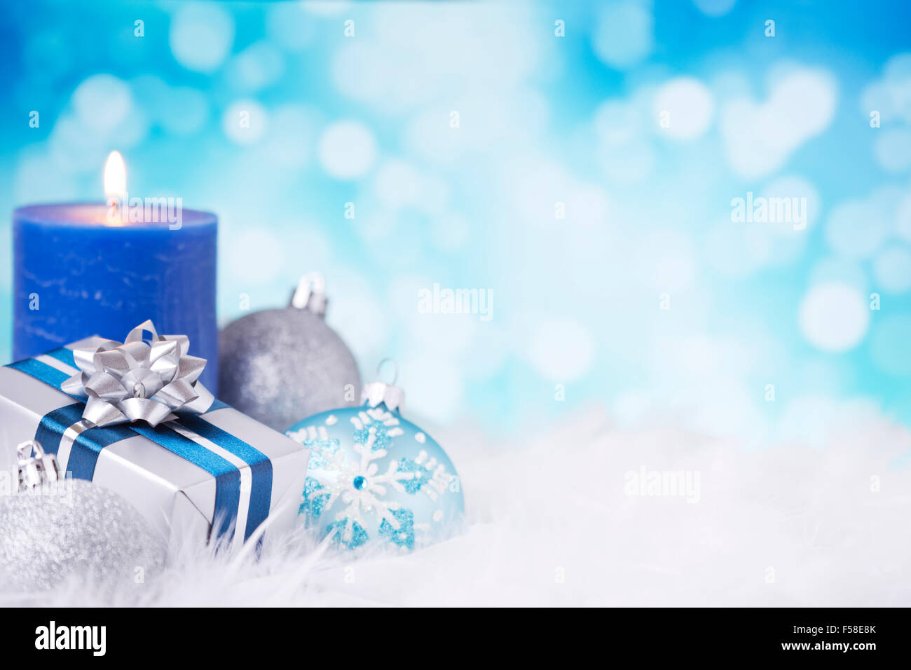 Blau und Silber Weihnachtskugeln, ein Geschenk und eine Kerze auf eine weiche federleichte Oberfläche vor defokussierten blaue und weiße Lichter. Stockfoto