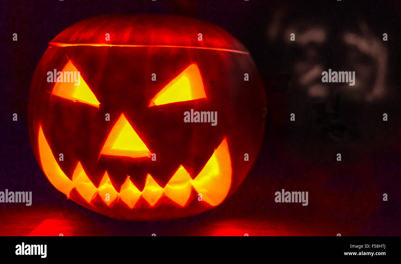 Scary Halloween Kürbis beleuchtet durch eine Kerze mit einem geisterhaften Gesicht Schatten hinter sich. Stockfoto