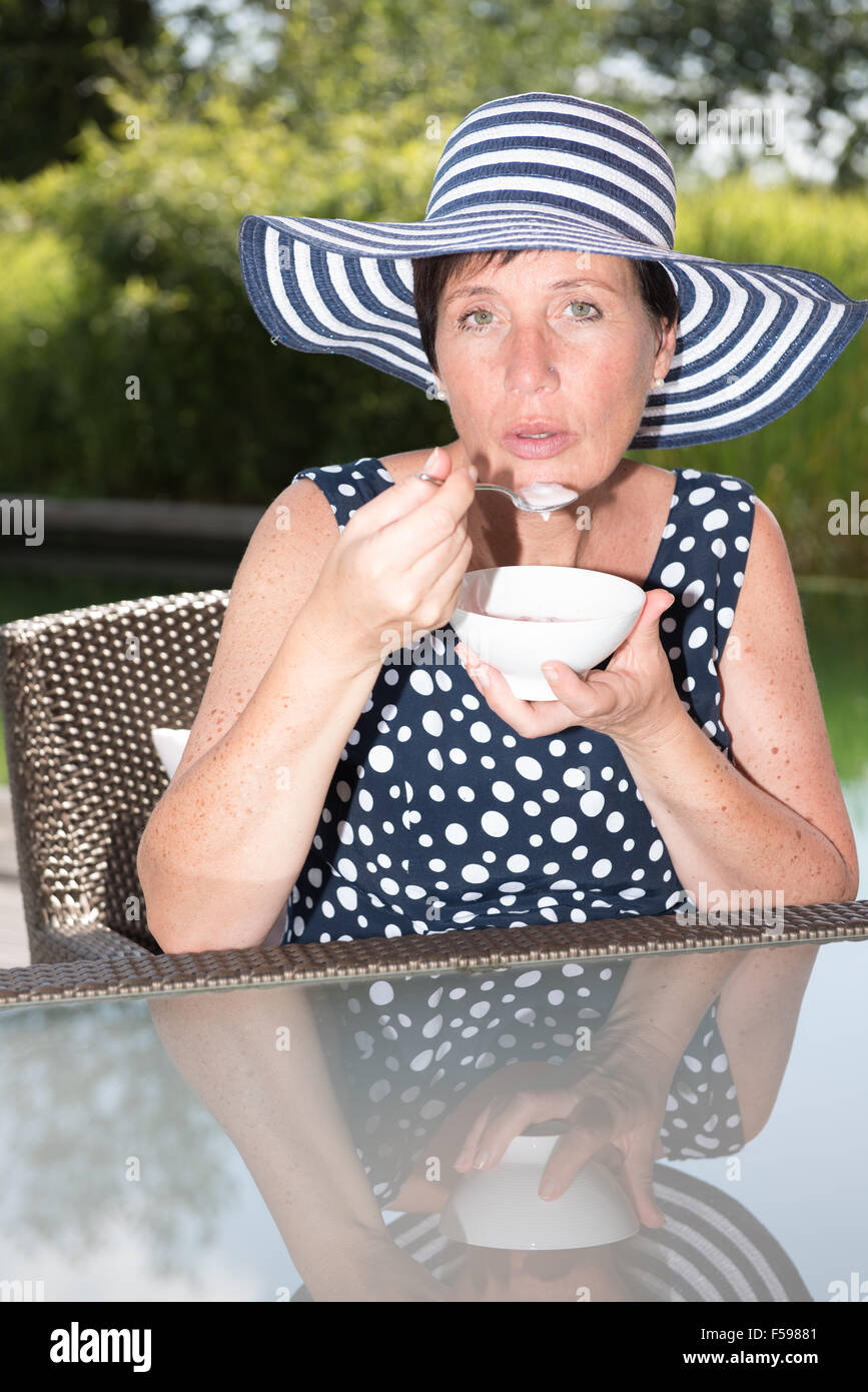 attraktive Frau aufgewirbelt am Pool und Essen eine Schale mit Obst Stockfoto