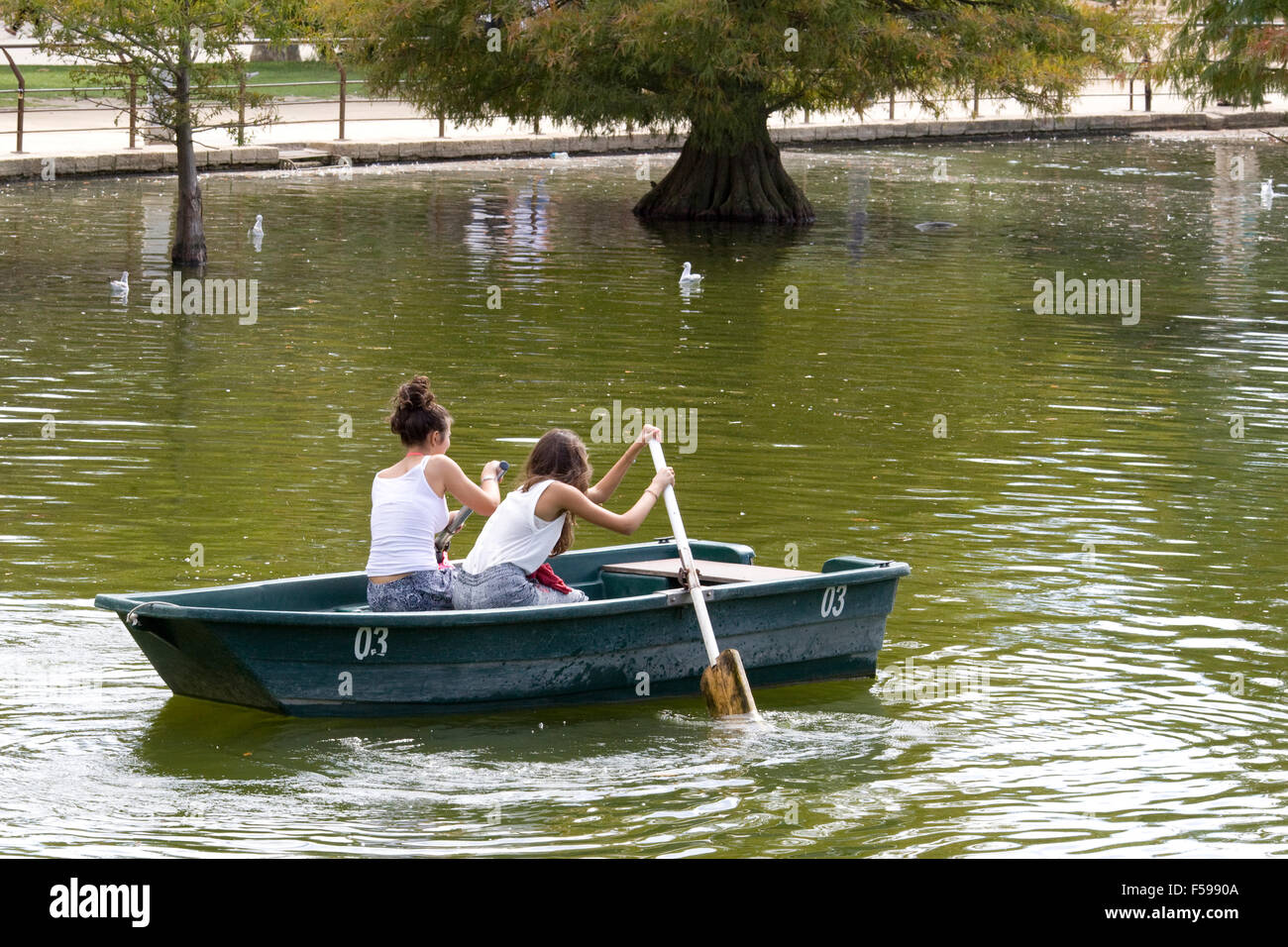 Zwei Mädchen, die versuchen, ein Paddelboot hinunter die Serpentine in London zu rudern Stockfoto