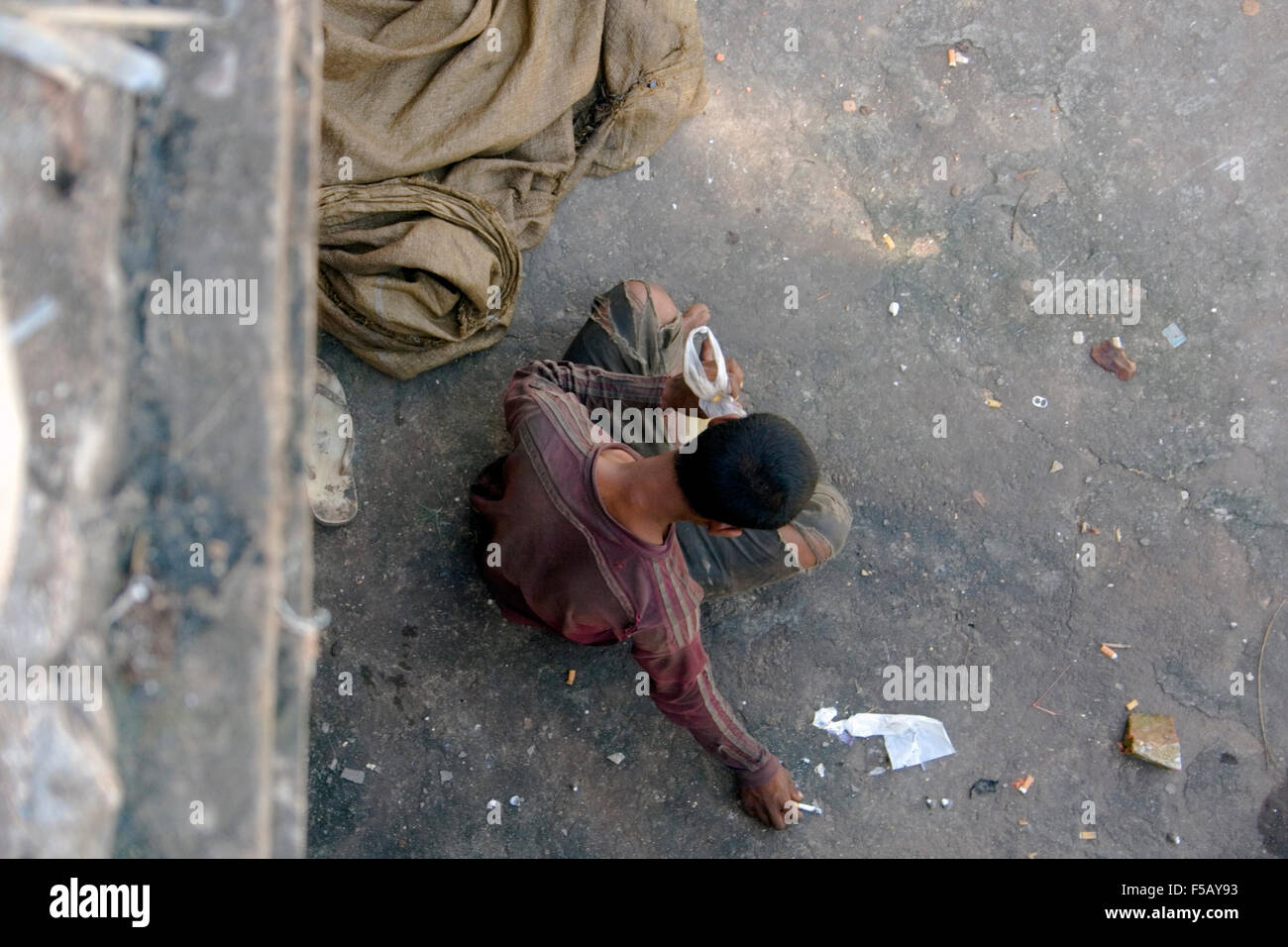 Ein Scavenger-Mann lebt in Armut sitzt auf einem Bürgersteig, während er Kleber schnüffelt & eine Zigarette in Kampong Cham, Kambodscha raucht. Stockfoto