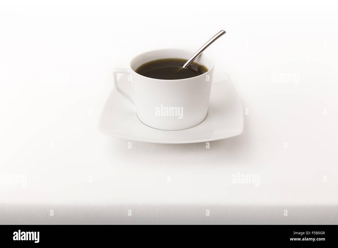 Eine moderne Tasse Tee mit einem Löffel auf ein weißes Tischtuch mit echten Schatten unten Stockfoto