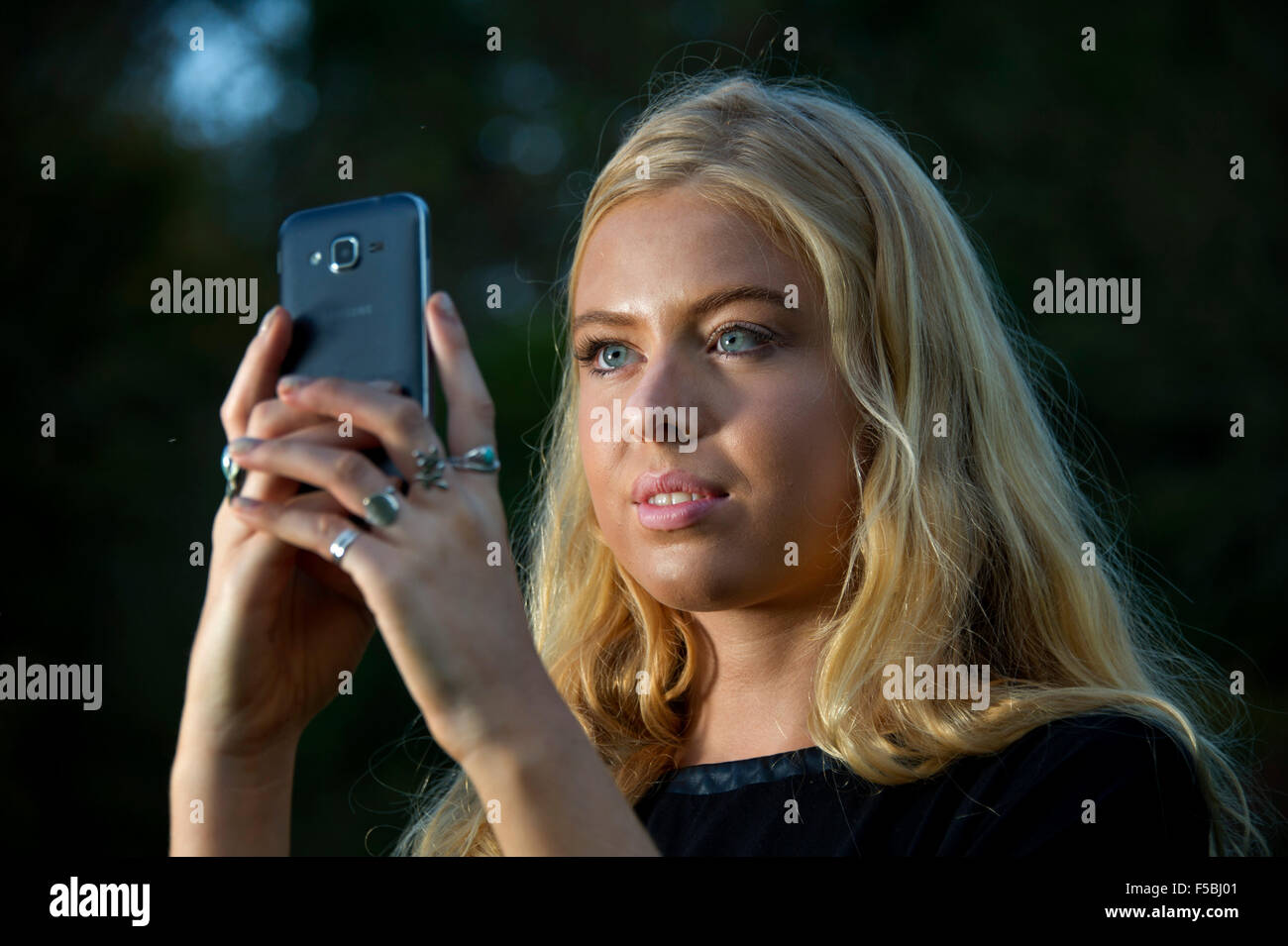Junge blonde Frau mit Handy im Dunkeln Stockfoto