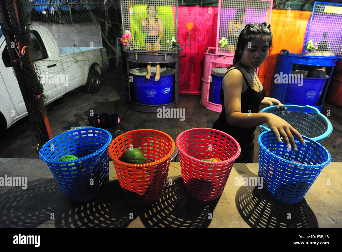 Bangkok, Thailand. 1. November 2015. Ein Verkäufer bereitet Kugeln da dunk Tank, die Mädchen hinter dem Netz in Bangkok, Thailand, 1. November 2015 sitzen. Ein Dunk Tank besteht aus einem Tank Wasser, über die ein Freiwilliger auf einem einstürzenden Sitz sitzt. Wenn ein Ball ein Ziel trifft, der Sitz bricht zusammen und "dunks" die Person ins Wasser. © Rachen Sageamsak/Xinhua/Alamy Live-Nachrichten Stockfoto