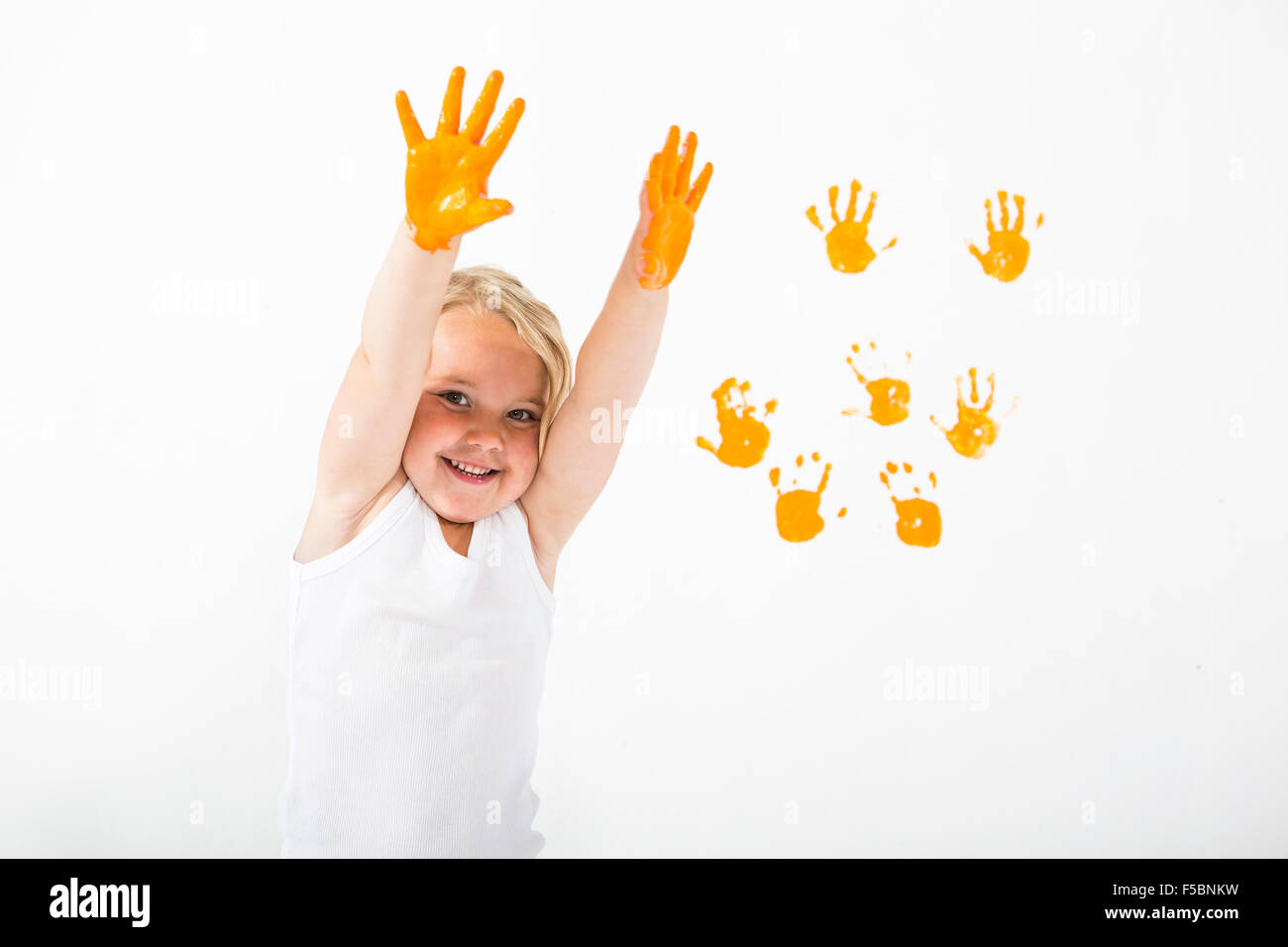 Kleine Mädchen malen weiße Wand mit orange Farbe und Handabdrücke Stockfoto