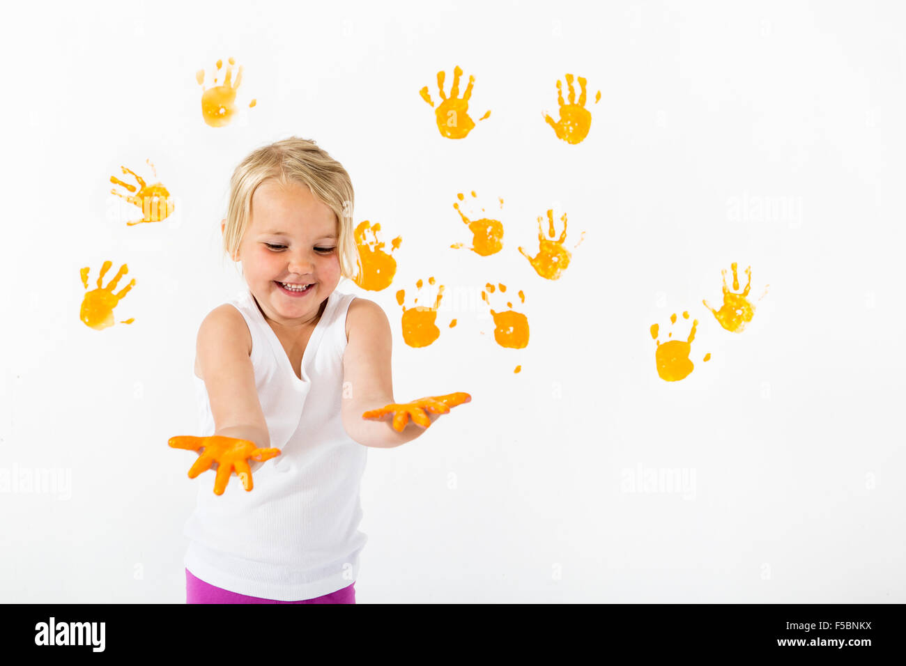 Kleine Mädchen malen weiße Wand mit orange Farbe und Handabdrücke Stockfoto