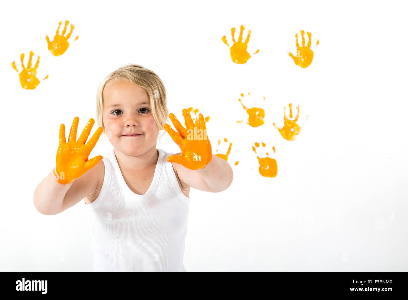 Kleine Mädchen malen weiße Wand mit orange Farbe und Handabdrücke Stockfoto