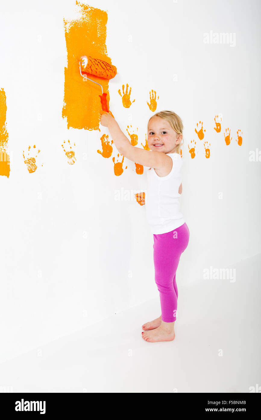 Kleine Mädchen malen weiße Wand mit orange Farbe Stockfoto