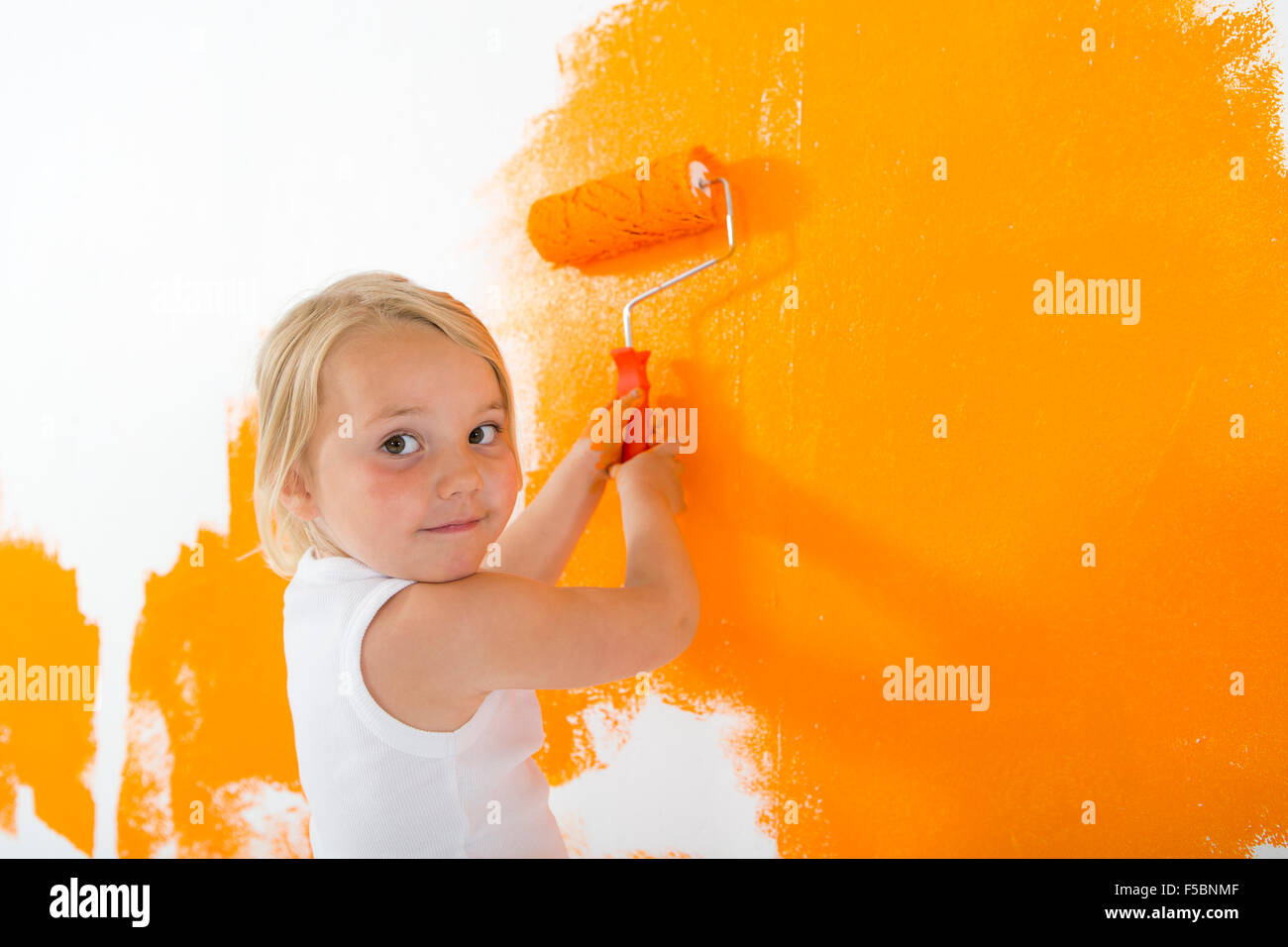 Kleine Mädchen malen weiße Wand mit orange Farbe Stockfoto